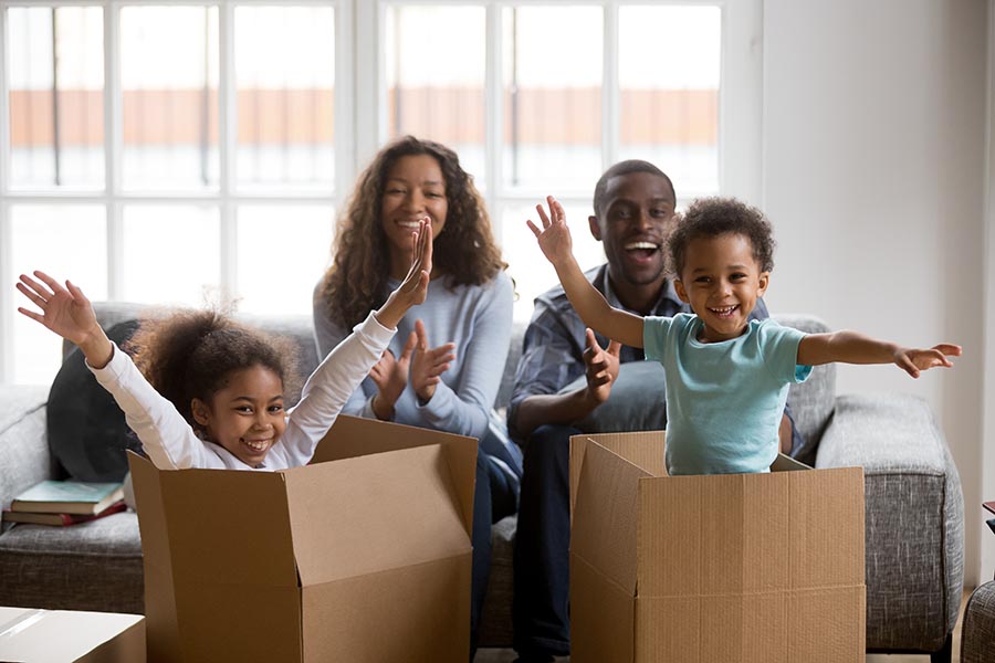 Blog - Family Celebrates Moving Into Their New Home, Kids Playing in Cardboard Boxes, Parents Clapping
