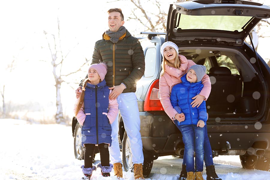Personal Insurance - Family in Winter Gear Stands Outside Their Car in a Light Snow on a Bright Sunny Day